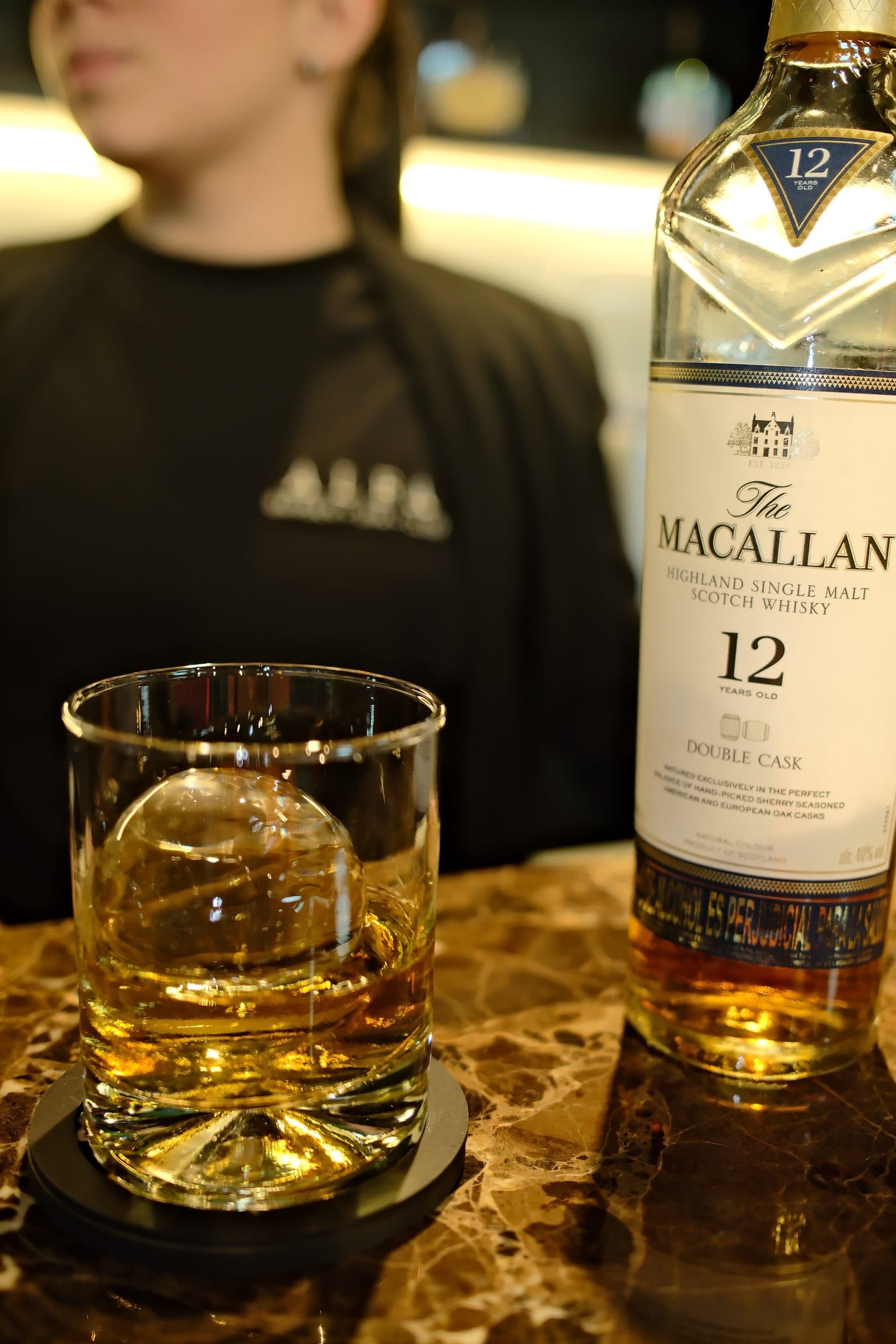 Vaso de whisky Macallan 12 servido con hielo esférico en la barra de ALFA Barber Spa Club