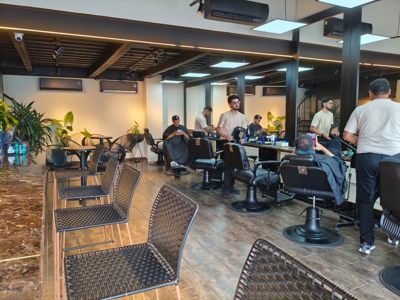 Salón de ALFA Barber Spa Club en Barranquilla: la barra de mármol en primer plano y, al fondo, los puestos de barbería con clientes atendiéndose